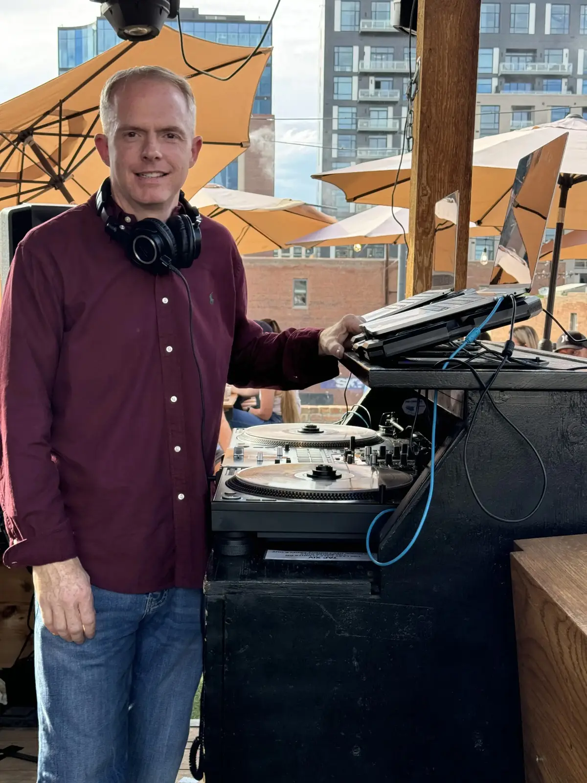DJ Thriller with vinyl turntables at Denver rooftop venue with city skyline and orange umbrellas